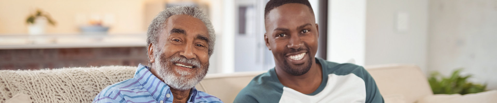 elder man with man caregiver smiling while sitting at the couch